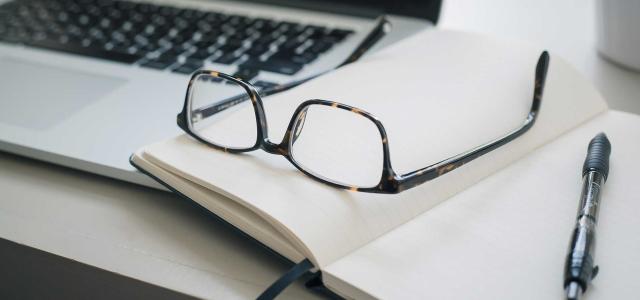 Glasses on a notebook, next to a laptop.